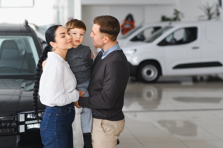 Happy parents with small kid after receiving keys for their new car in a showroom. Congratulations, we have a deal about buying a car! Happy family came to an agreement with a car salespersonの写真素材
