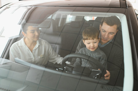 A joyful family sitting inside a new car at a dealership, with parents and child excitedly exploring...