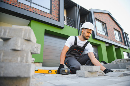 The master in gloves lays paving stones in layers. Garden brick pathway paving by professional paver...