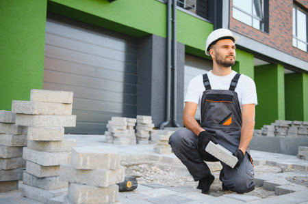 Worker skillfully laying paving stones using a hammer and wearing gloves, showcasing precision.の写真素材