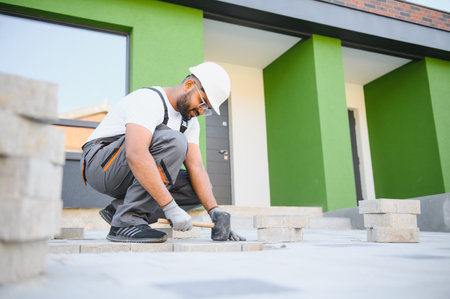 Indian master in gloves lays paving stones in layers. Garden brick pathway paving by professional...