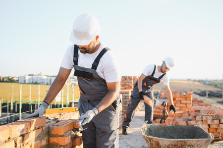 A team of Indian construction workers in overalls and hard hats are building a brick wall.