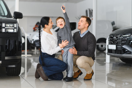 Happy parents with small kid after receiving keys for their new car in a showroom. Congratulations, we have a deal about buying a car. Happy family came to an agreement with a car salespersonの写真素材