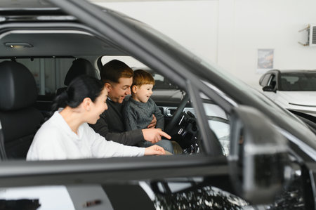 A joyful family sitting inside a new car at a dealership, with parents and child excitedly exploring features. Perfect image for concepts of family, happiness, and car shopping.の写真素材