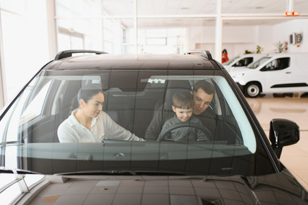 A joyful family sitting inside a new car at a dealership, with parents and child excitedly exploring features. Perfect image for concepts of family, happiness, and car shopping.の写真素材