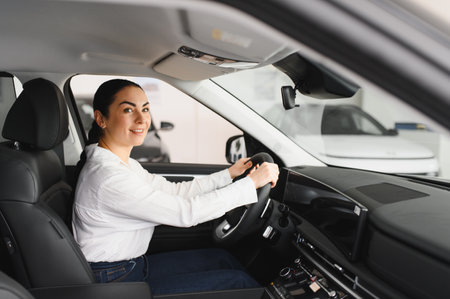 Cheerful female client of car dealership smiling and looking at camera while sitting inside new red...