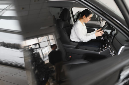 Cheerful female client of car dealership smiling and looking at camera while sitting inside new red...