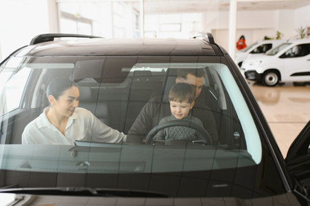 A joyful family sitting inside a new car at a dealership, with parents and child excitedly exploring features. Perfect image for concepts of family, happiness, and car shopping.の写真素材