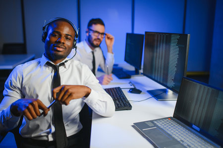 Happy Confident Technical Customer Support Specialist Having a Headset Call in a Monitoring and Control Room Filled with Colleagues and Display Screens.の写真素材