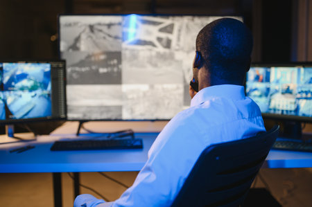 Back view of African-American security operator use computer with screens showing surveillance camera footage.の写真素材