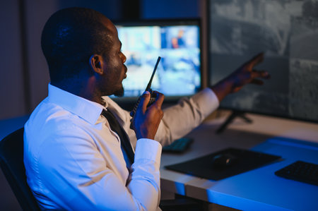 African-American security officer watching the screens talking on radio in control room.