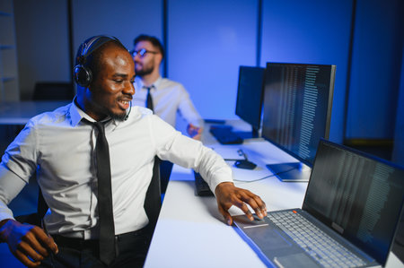 Happy Confident Technical Customer Support Specialist Having a Headset Call in a Monitoring and Control Room Filled with Colleagues and Display Screens.の写真素材