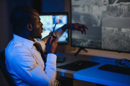 Back view of African-American security operator use computer with screens showing surveillance camera footage.の写真素材