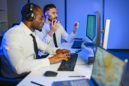 Male Data Scientist Works on Personal Computer Wearing a Headset in Big Infrastructure Control and...