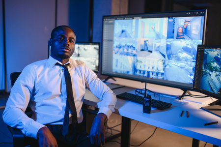African-American security officer watching the screens talking on radio in control room.