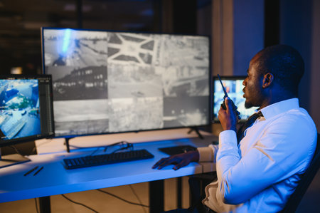 African-American security officer watching the screens talking on radio in control room.の写真素材