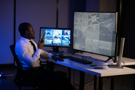 African American security officer or dispatch uses computer and walkie talkie, looks at screens.の写真素材
