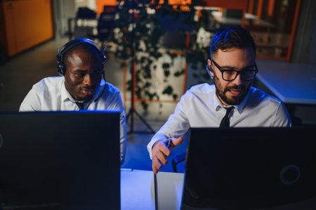 Male Data Scientist Works on Personal Computer Wearing a Headset in Big Infrastructure Control and Monitoring Room. Young Engineer in a Business Call Center Office Roomの写真素材