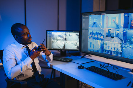 African-American security officer watching the screens talking on radio in control room.