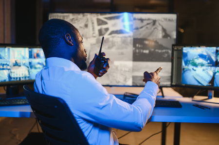 Back view of African-American security operator use computer with screens showing surveillance...