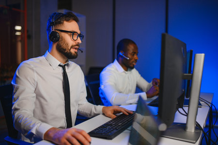 Male Data Scientist Works on Personal Computer Wearing a Headset in Big Infrastructure Control and...