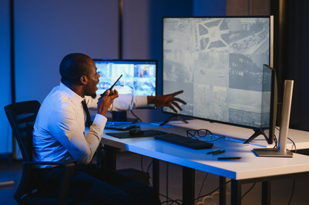 African-American security officer watching the screens talking on radio in control room.の写真素材