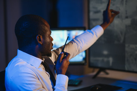 Back view of African-American security operator use computer with screens showing surveillance...
