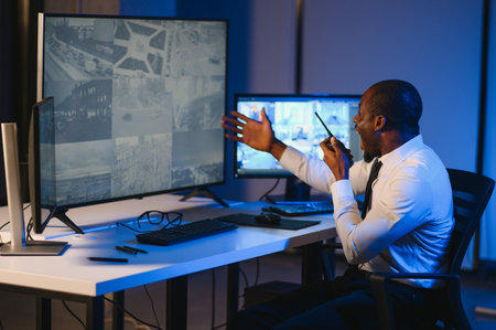 Serious African American security guard watching cctv video in surveillance room while observing...