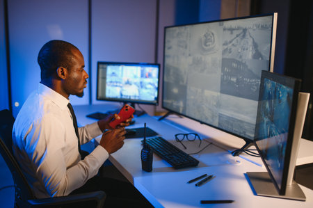 Serious African American security guard watching cctv video in surveillance room while observing hotel life on computer screenの写真素材