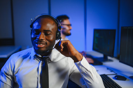 Male Data Scientist Works on Personal Computer Wearing a Headset in Big Infrastructure Control and Monitoring Room. Young Engineer in a Business Call Center Office Roomの写真素材
