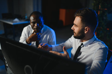 Financial Analyst Talking to Investment Banker in the Evening at Work. Chatting About Real Time Stock Chart Data on Multi Monitor Workstationの写真素材