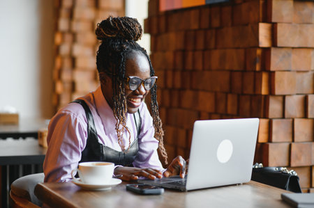 Beautiful black businesswoman sitting in restaurant or cafe bar and using her laptop.の写真素材