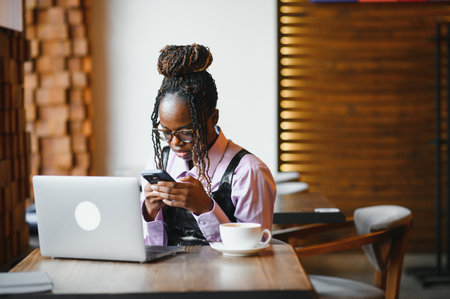 Beautiful black businesswoman sitting in restaurant or cafe bar and using her laptop.の写真素材