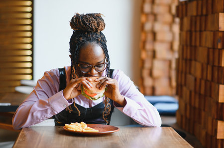 African woman with afro hair eating a tasty classic burger with fries. Cheat Meal.の写真素材