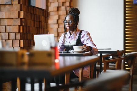 Focused young African woman sitting alone at a counter in a cafe.の写真素材