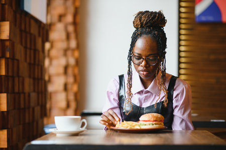 African girl eating burger and fries in cafe. Fast food concept.の写真素材