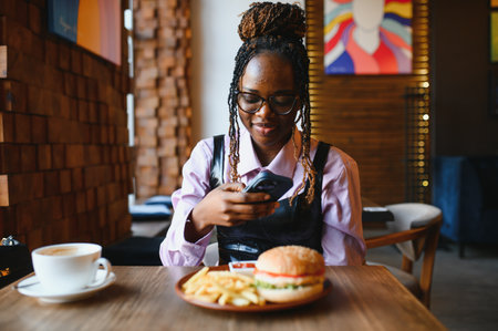 African girl taking a picture of a burger before eating in a cafe.の写真素材