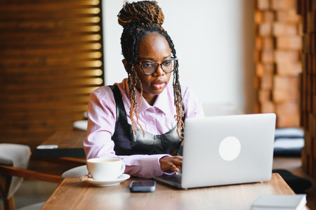 Portrait of smart young woman with mobile phone working on laptop at outdoor coffee shop.の写真素材