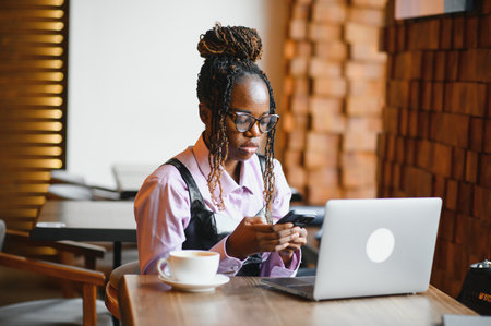 Focused young African woman sitting alone at a counter in a cafe.の写真素材