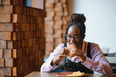 African woman with afro hair eating a tasty classic burger with fries. Cheat Meal.の写真素材