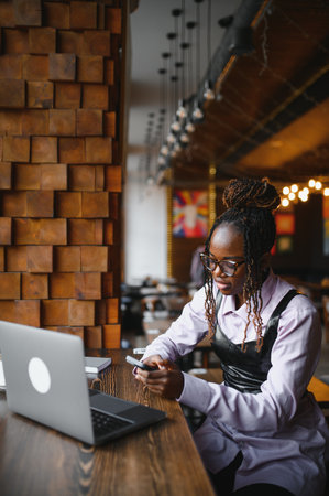 Happy young black woman using laptop in cafe.の写真素材