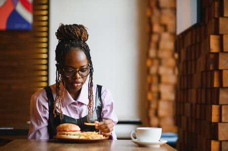 African woman with afro hair eating a tasty classic burger with fries. Cheat Meal.の写真素材
