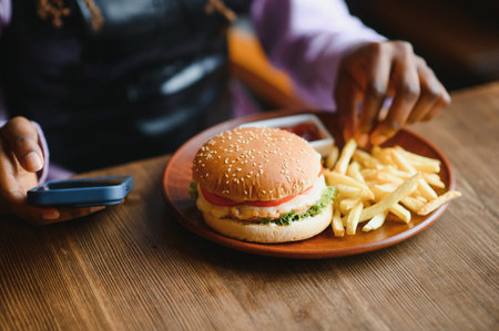 African woman with afro hair eating a tasty classic burger with fries. Cheat Meal.の写真素材