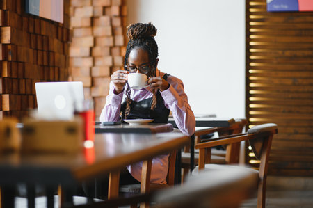 Portrait of an African American young woman sitting at cafe with laptop writing her blog.の写真素材
