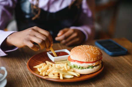 African woman with afro hair eating a tasty classic burger with fries. Cheat Meal.の写真素材