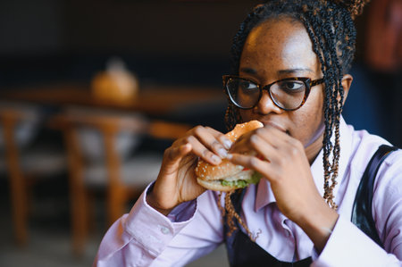 African girl eating burger and fries in cafe. Fast food concept.