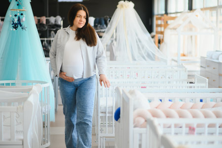 Happy pregnant woman choosing a baby crib in the store.