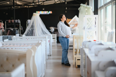 Happy pregnant woman choosing a baby crib in the store.