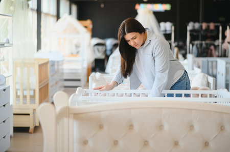 Pregnancy shopping concept. Pregnant woman choosing cradle cot or crib for newborn at baby shop store.の写真素材
