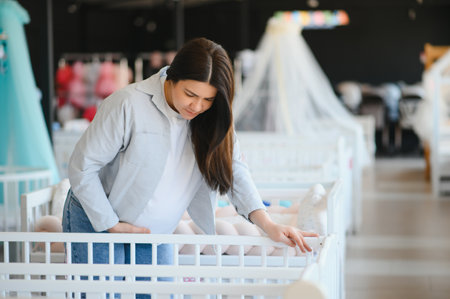 Pregnancy shopping concept. Pregnant woman choosing cradle cot or crib for newborn at baby shop store.の写真素材
